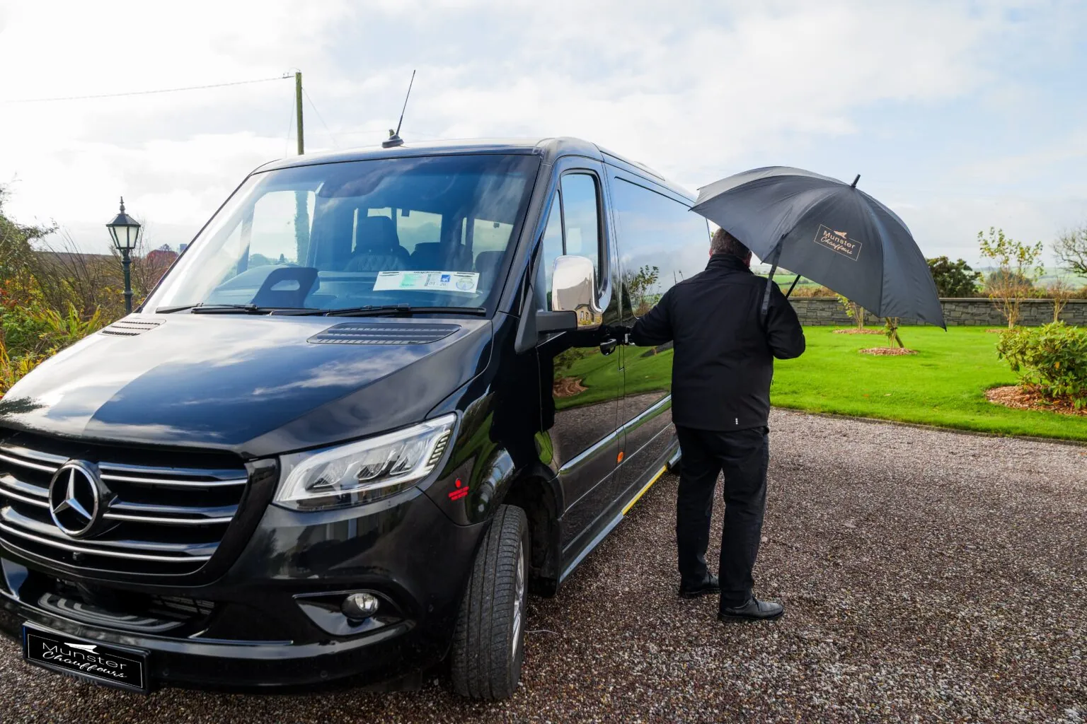 Chauffeur opening door with umbrella for golf trip clients